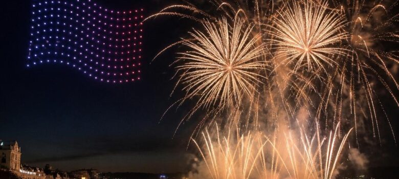 Drones dessinant le drapeau français à côté d’un feu d’artifice sur une baie
