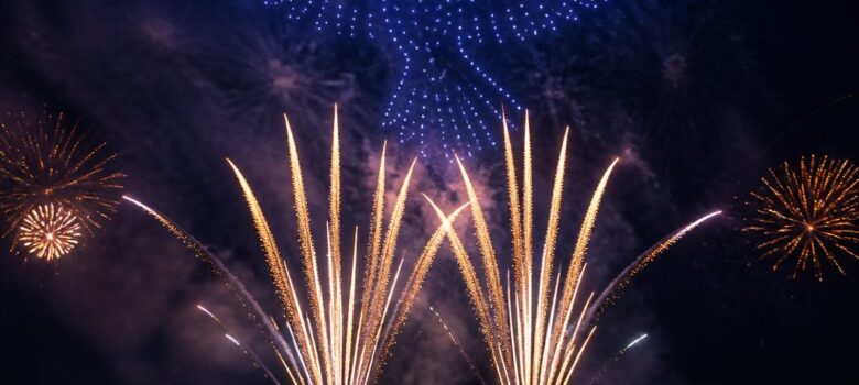 Grand oiseau bleu formé par des drones au-dessus de gerbes pyrotechniques dorées